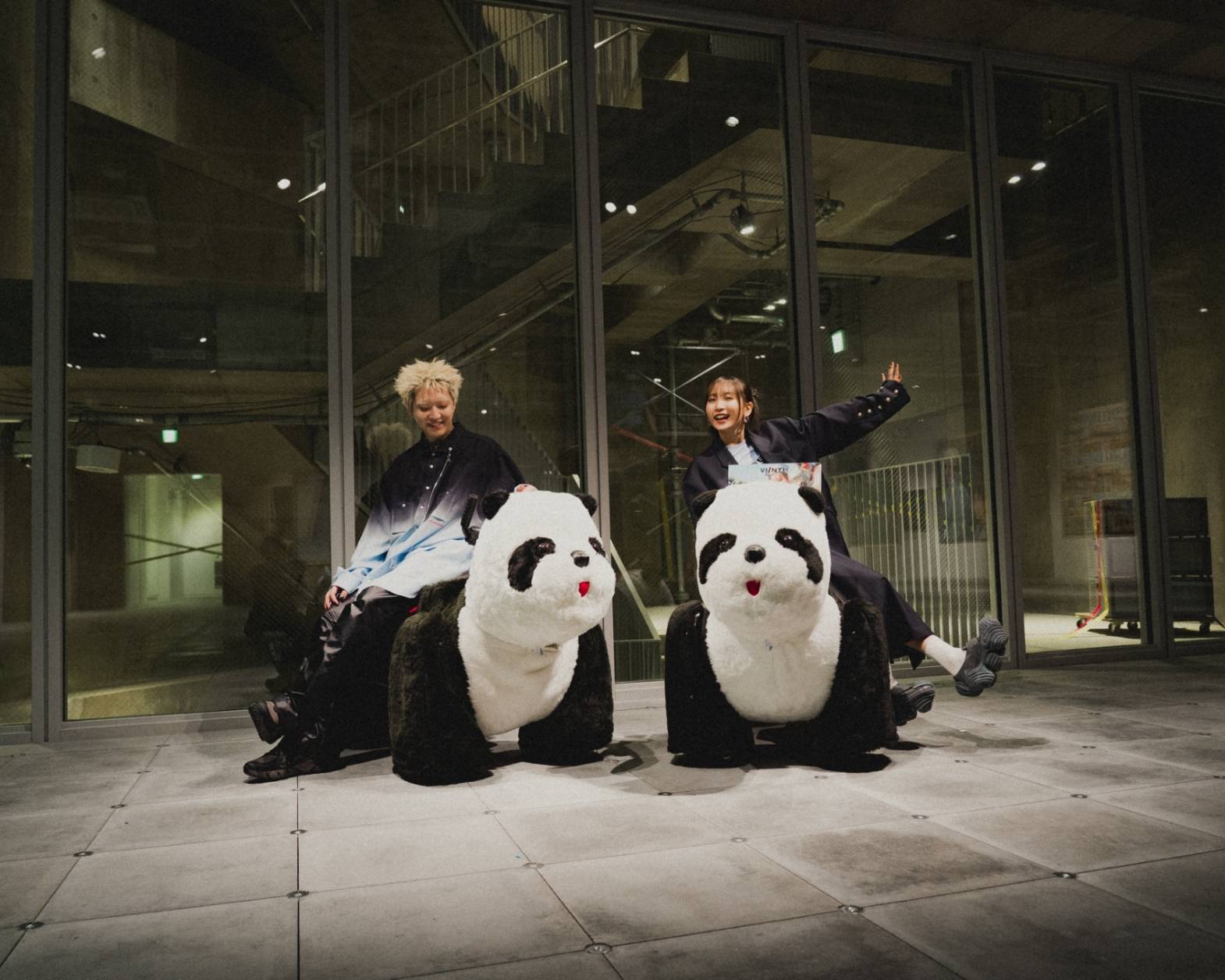 A hands-on experience. The two members of YOASOBI posing while riding large panda props.
