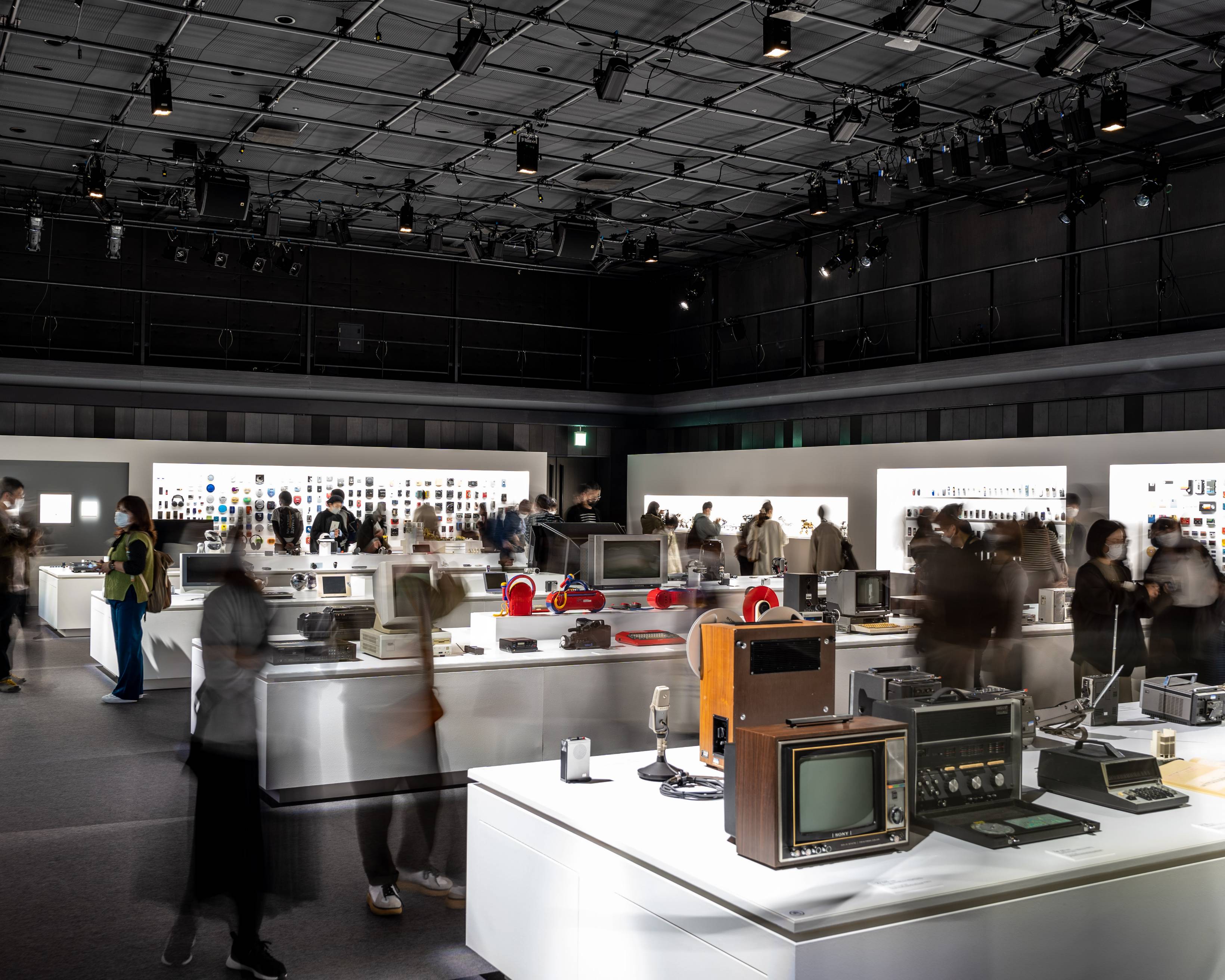 Exhibit. An exhibit of many past Sony products, with Trinitron color TVs on the exhibition stand in the foreground, My First Sony products near the center, and WALKMAN models on the back wall.
