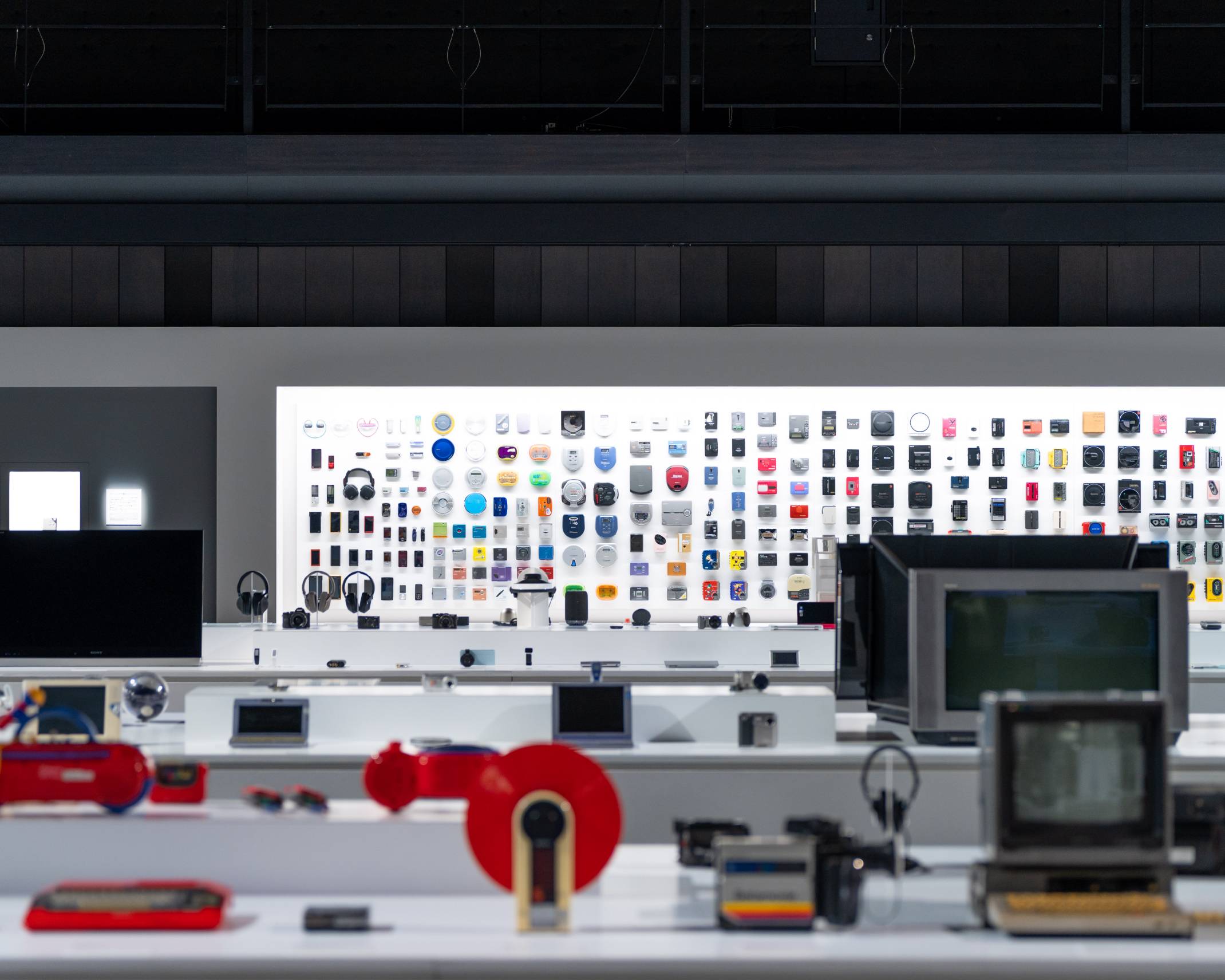 Exhibit. A variety of WALKMAN models from over the years are exhibited on the back wall, past multiple rows of display stands.