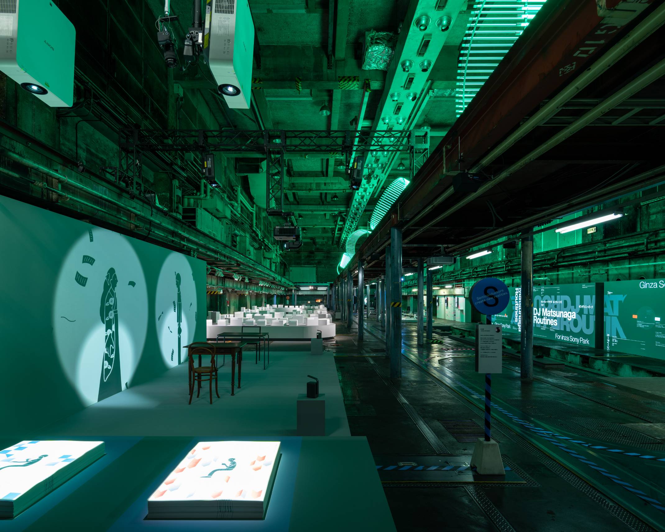 Exhibit. Animated shadow puppets are projected onto the wall in a space lit with green lighting.