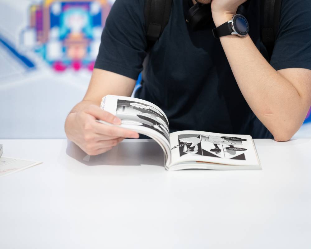 A hands-on experience. A visitor reads a physical manga at a table in front of the large wall exhibits.