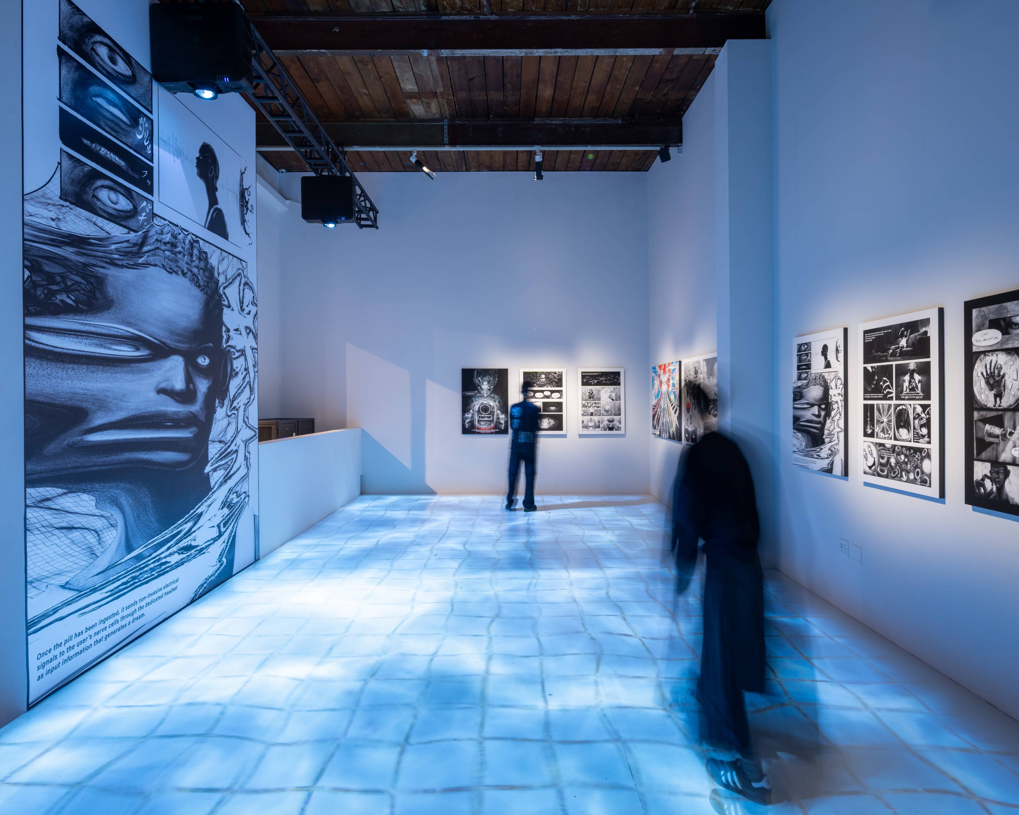 Exhibit. Individual pages from the manga DREAM PILL are exhibited on the walls, and an image of tiles covered in water has been projected onto the floor.