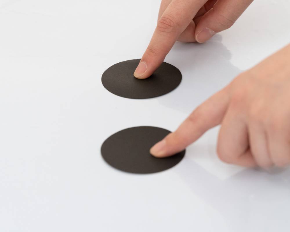 A hands-on experience. A person places both of their index fingers on two black circles on a sheet.