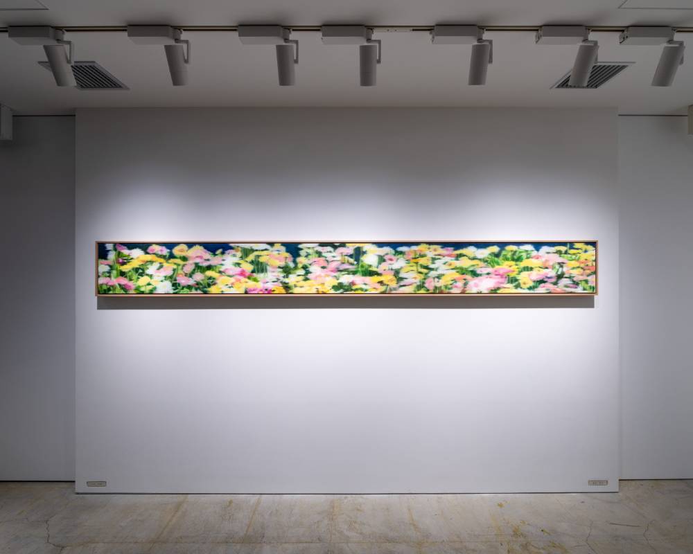 Exhibit. A horizontal art piece depicting a field of gerbera daisies is displayed on the wall.