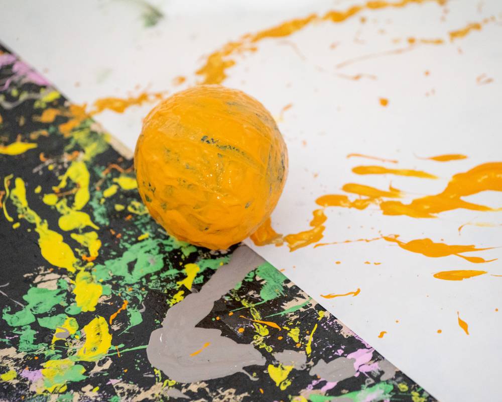 Art piece in production. A spherical stone ball covered in orange paint lies on top of a drawing.