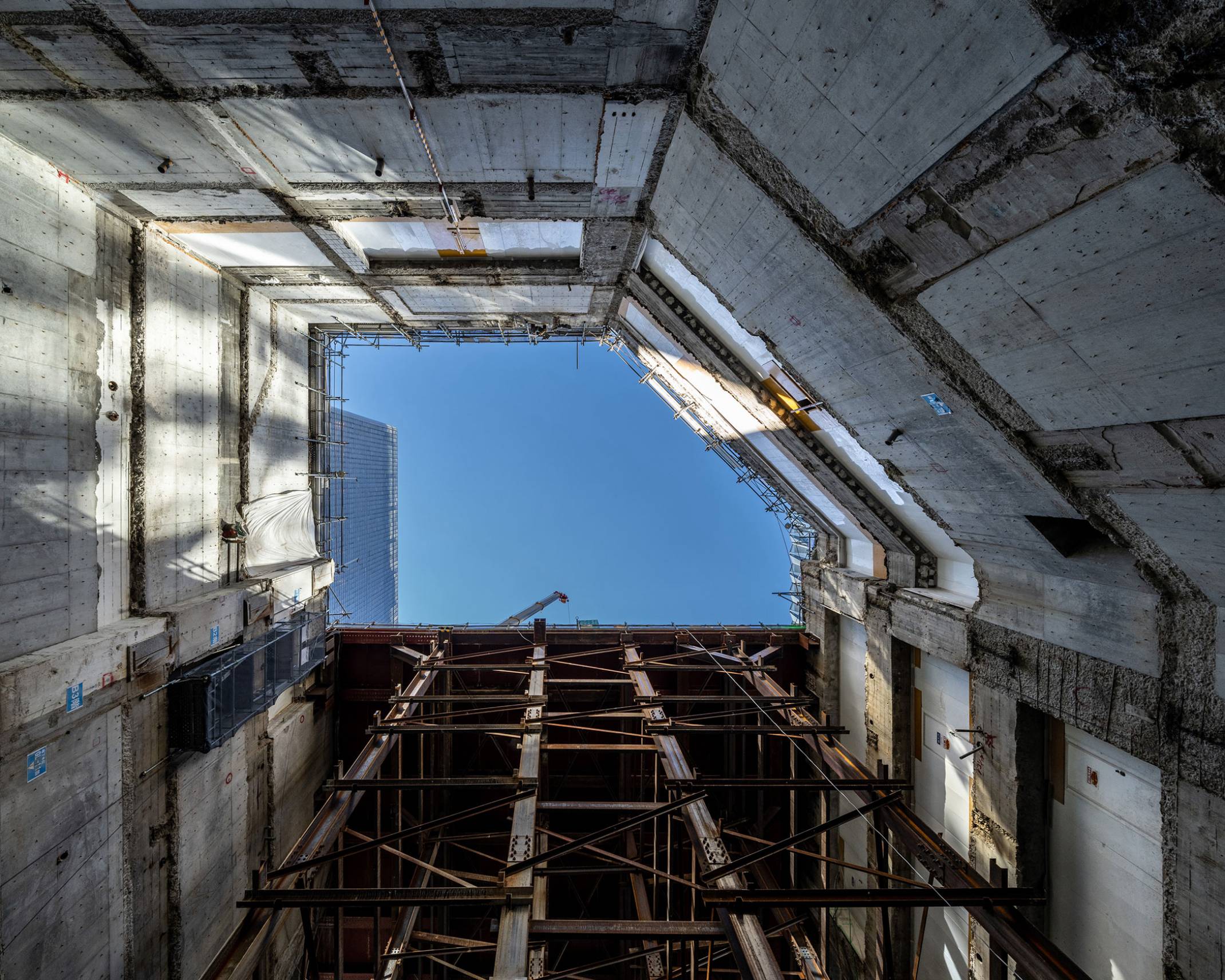 Record of the new building construction, inside view. Sky as seen from deep underground, ringed by the exterior basement walls and construction platform.