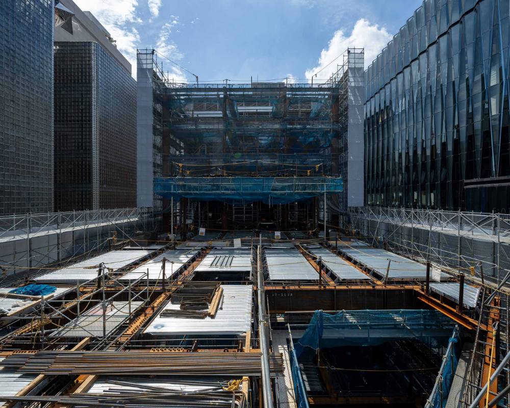 Record of the new building construction, exterior view. Construction site for the building frame on the rooftop floor, surrounded by scaffolding, prior to concrete pouring. The floor shows the exposed steel frame and deck.